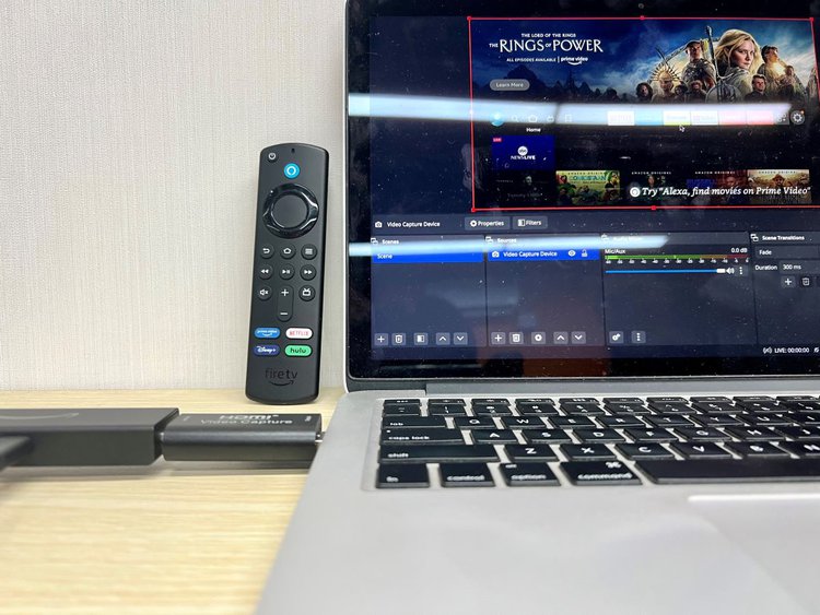 fire tv stick and a capture card are plugged into a macbook with fire remote standing next to it