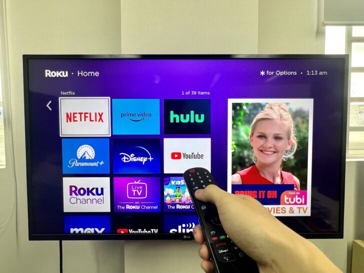 a hand holding a roku remote and pointing towards an lg tv