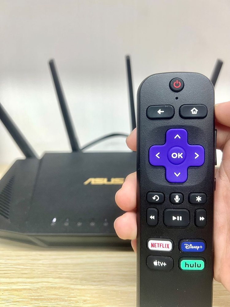a hand holding a roku remote in front of a router