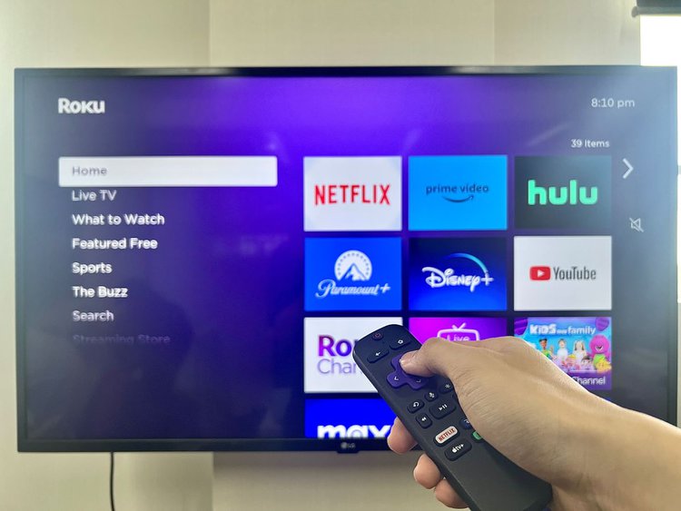 a hand holding a roku remote in front of an lg tv with roku plugged in