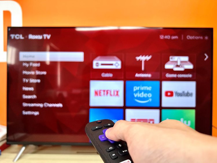 a hand holding a roku remote pointing at a roku tcl tv