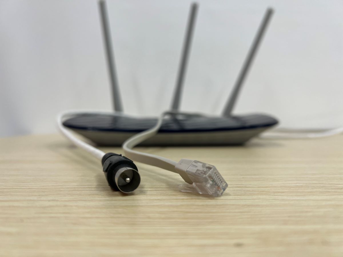 A coaxial cable and an ethernet cable side by side with the TP-Link router at the back