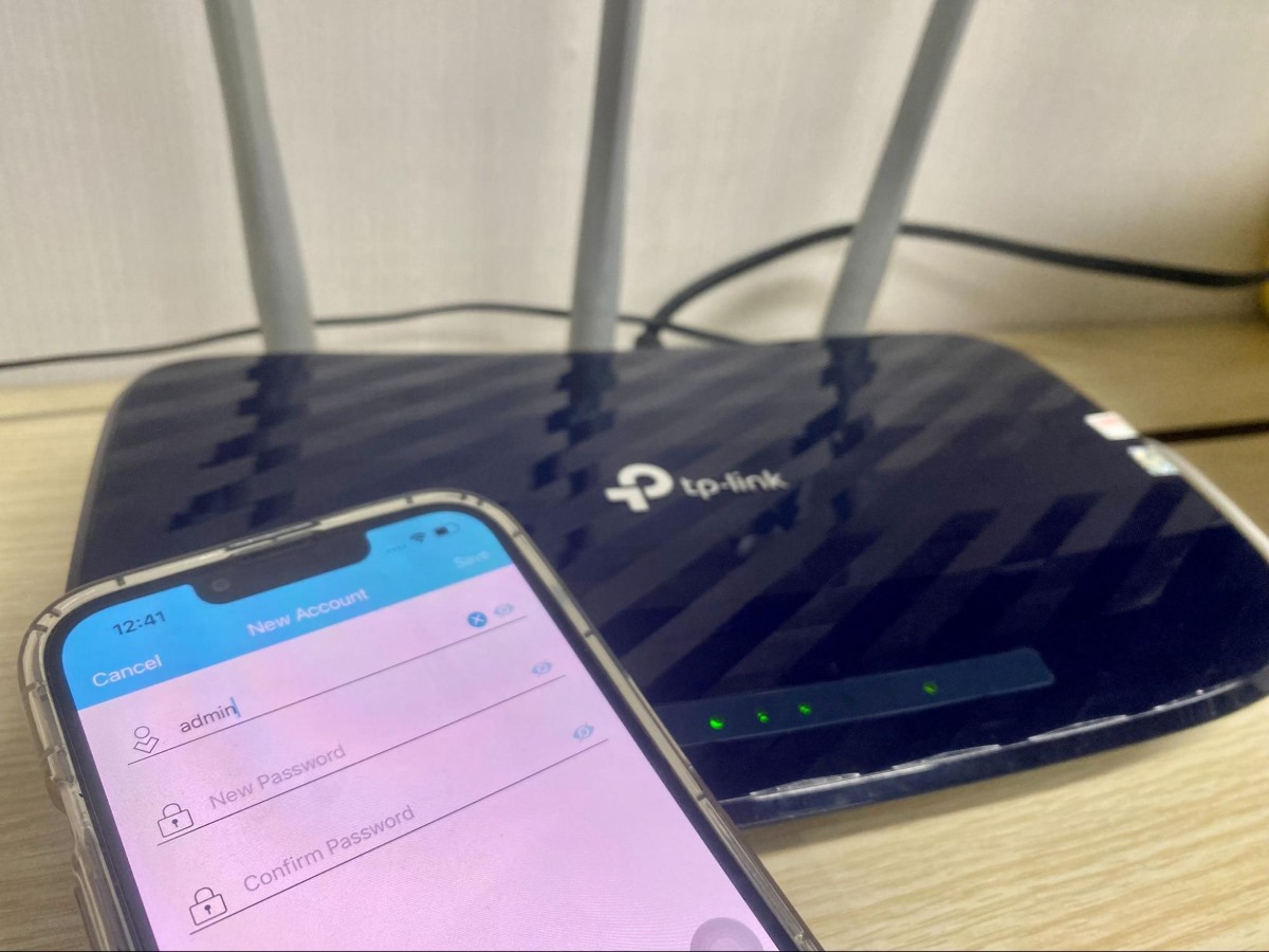 TP-Link Tether app with the password change screen on an iPhone placed in front of a TP-Link router