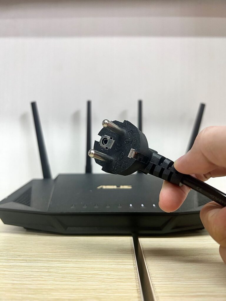 a hand holding a plug in front of an asus router