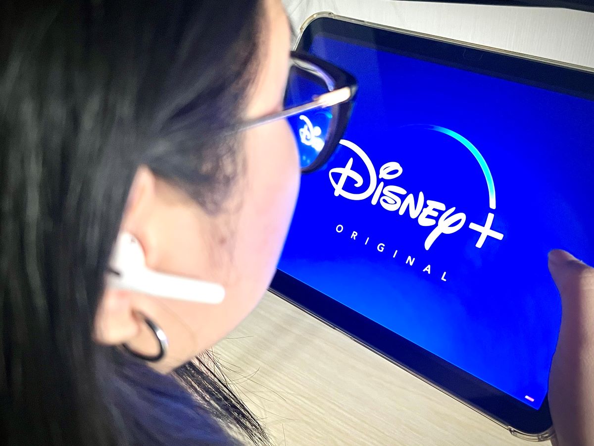 a girl wearing an airpods and turning on disney plus on an ipad