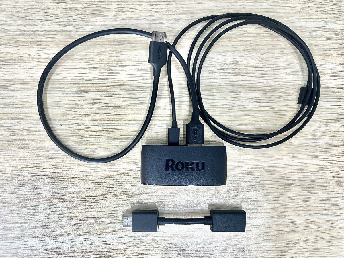 a roku express plugged in with power and hdmi cables is on a table with the hdmi extender right below