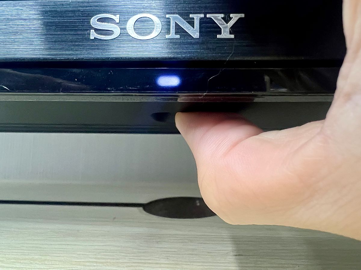 a hand holding sony tv's power button