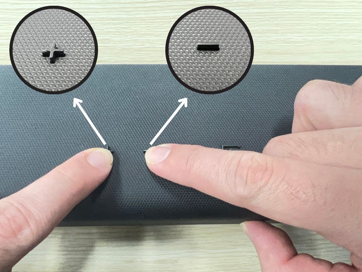 two hands are pressing the plus and minus buttons on Vizio soundbar