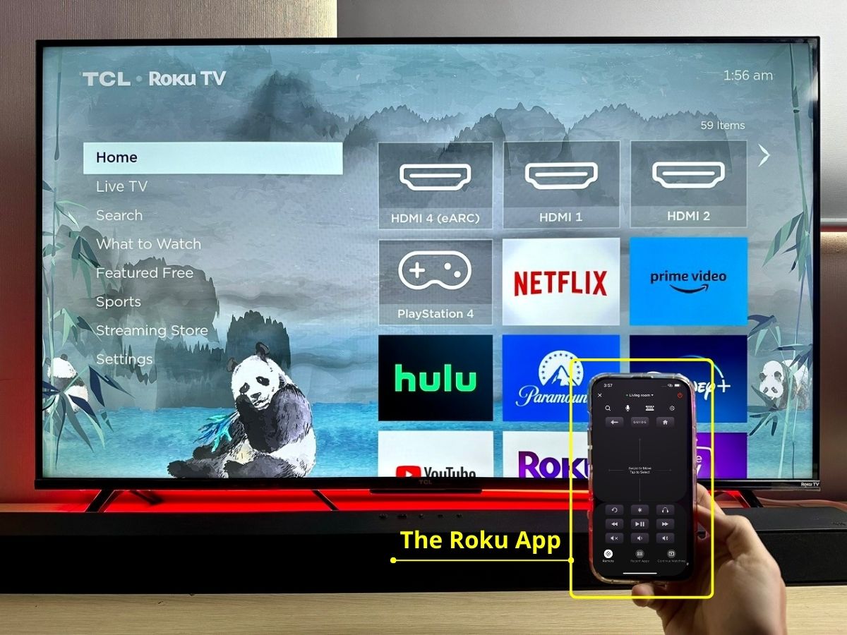 a hand holding a phone opening the roku app in front of a tcl roku tv